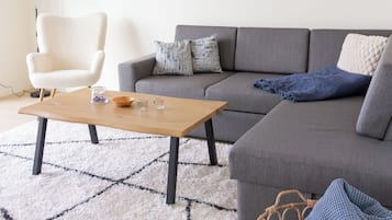 Un salon moderne avec un canapé gris, un fauteuil blanc, une table basse en bois et un tapis à motifs.