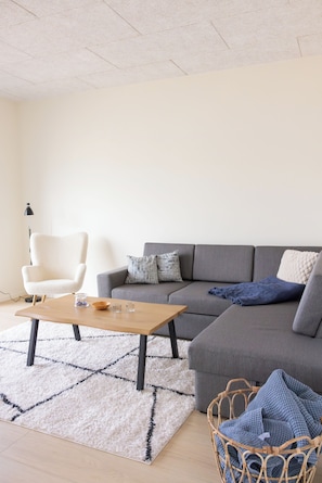 Una sala de estar moderna con un sofá gris, un sillón blanco, una mesa de centro de madera y una alfombra estampada.