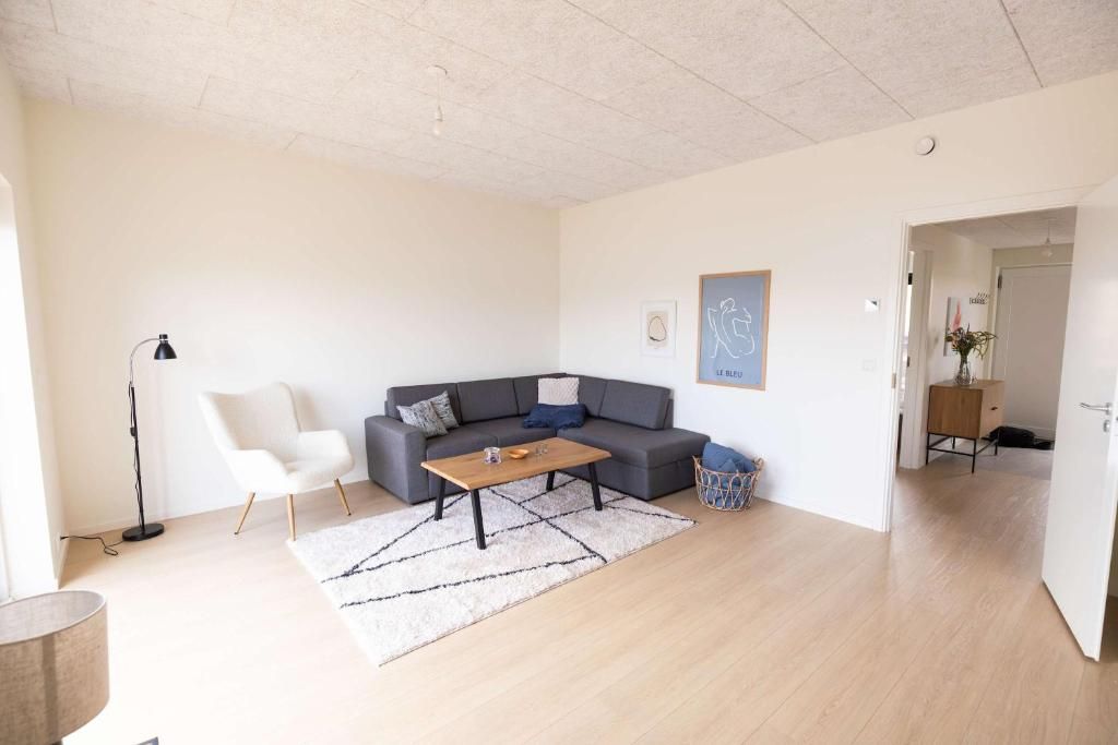 A modern living room with a grey sofa, a wooden coffee table, a white armchair, and a floor lamp.