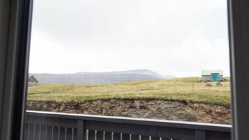 A view of a rural landscape with a stone wall, a fenced field, and a distant mountain range.
