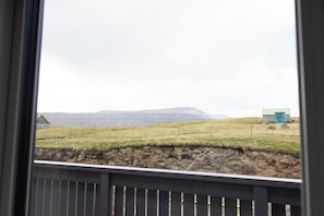A view of a rural landscape with a stone wall, a fenced field, and a distant mountain range.