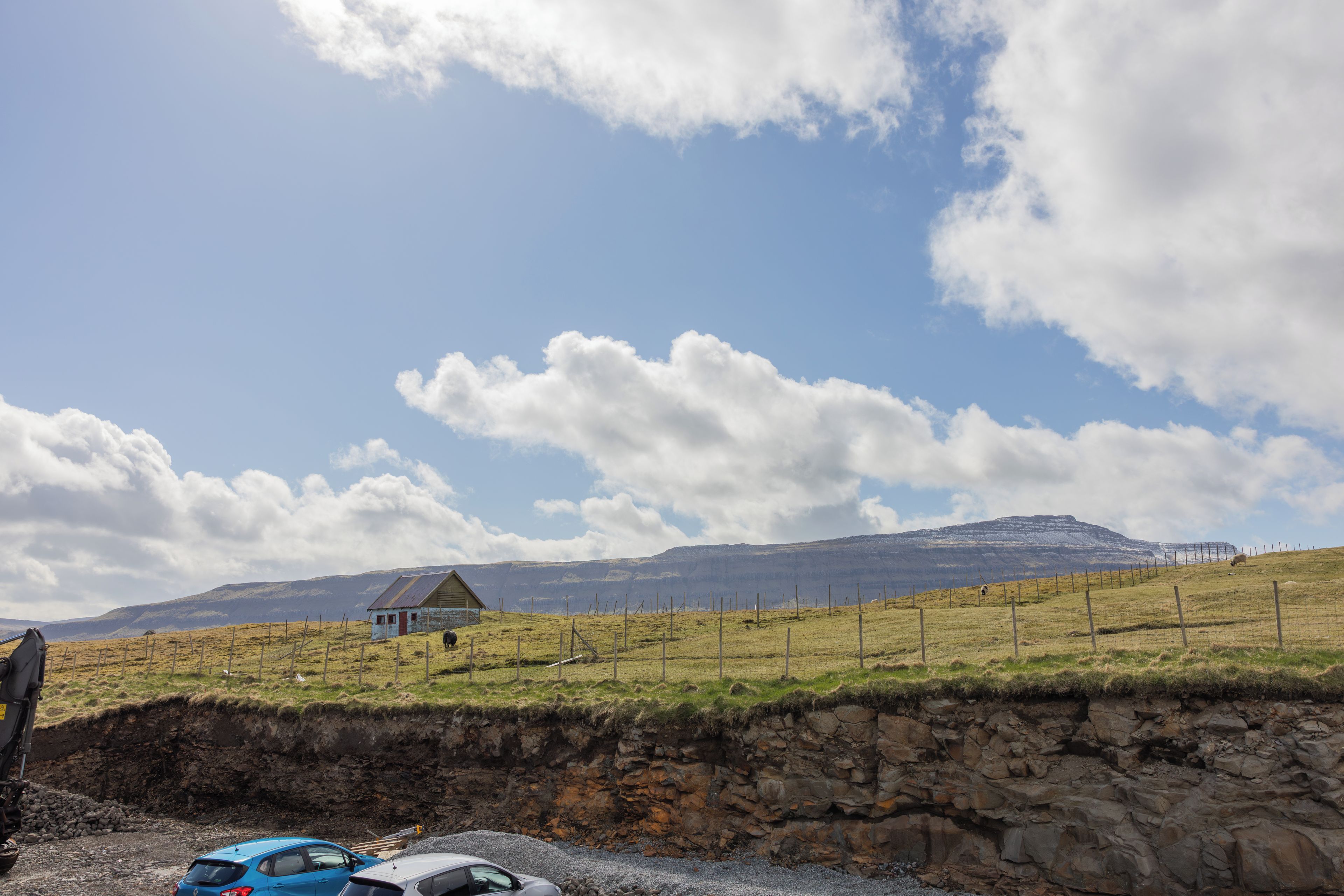 A rural landscape with a stone wall, a small house, and a fenced field.