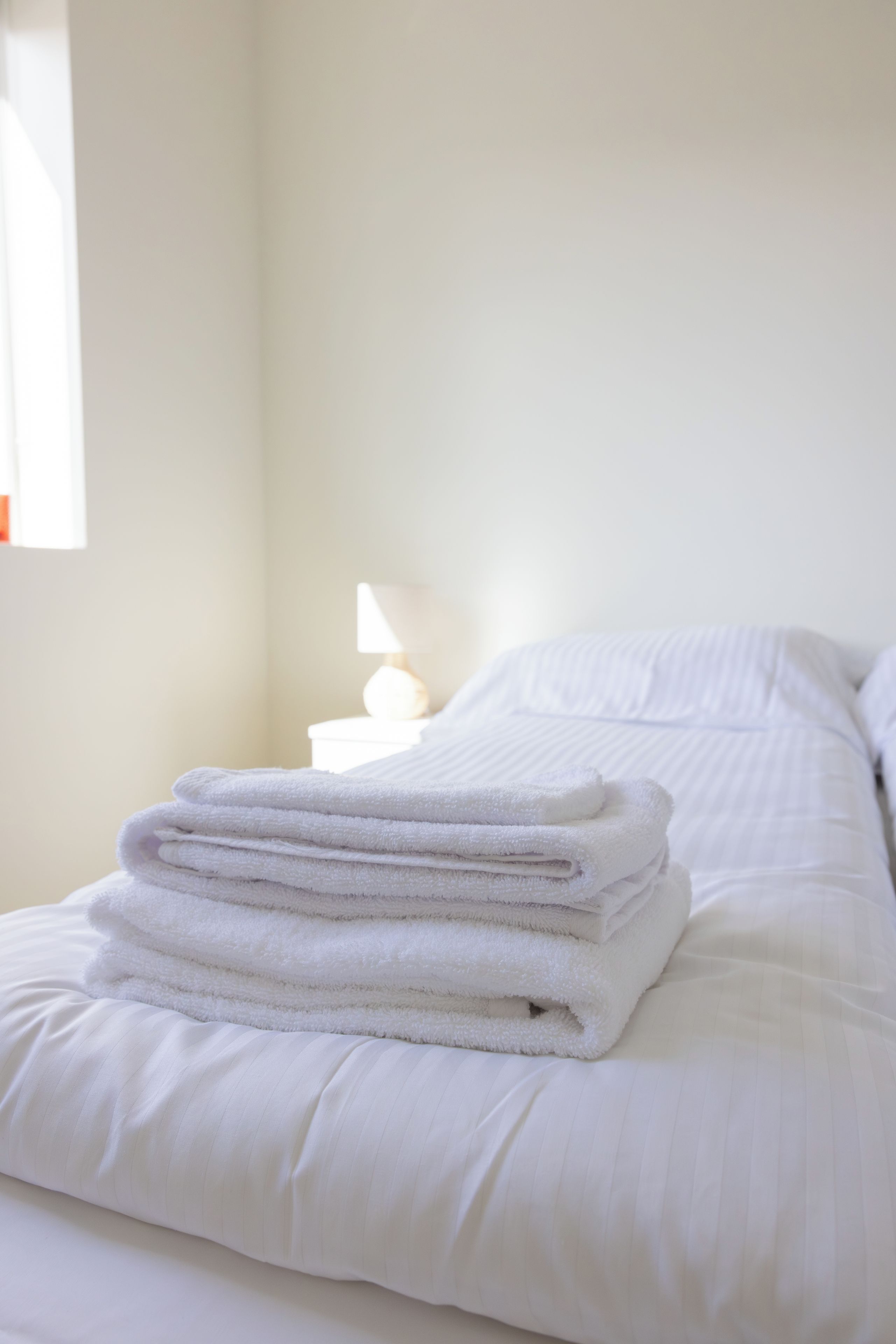 A neatly made bed with white linens and a stack of folded towels on the side.