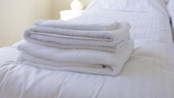 A neatly made bed with white linens and a stack of folded towels on the side.
