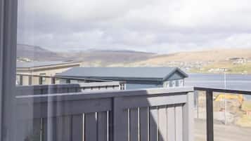 A view from a window overlooking a deck with a railing, a body of water, and distant hills.