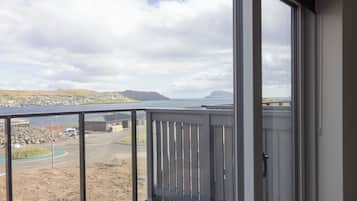 Un balcone con vista su una cittadina costiera, un corso d'acqua e colline lontane.