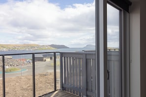 A balcony with a view of a coastal town, a body of water, and distant hills.