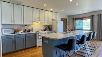 A modern kitchen with a central island, bar stools, and a large window.