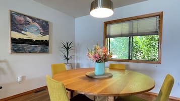 A dining area with a round wooden table, green upholstered chairs, a vase with flowers, and a painting on the wall.