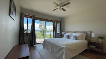 A bedroom with a bed, bedside tables, a ceiling fan, and a view of a lake through large windows.