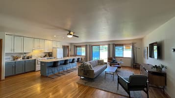 A spacious living area with a kitchen, a dining area, and a large window offering a view of the outdoors.