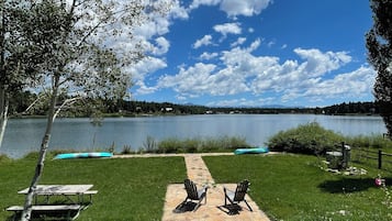 A lakeside deck with a picnic table and chairs, a clear view of the lake, and a distant mountain range.