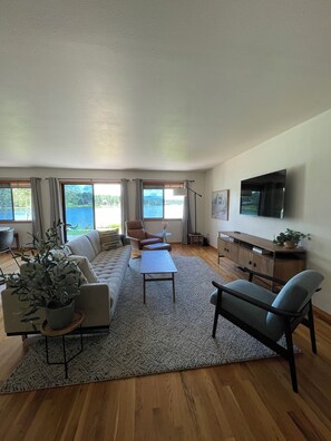 A spacious living room with a sofa, coffee table, and chairs, large windows with curtains, a flat-screen TV, and a view of a body of water. - Serene 3-bedroom house in Pagosa Springs perfect for your getaway (Pagosa Springs)