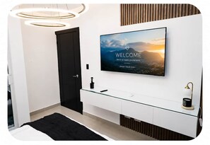 Un baño moderno con un espejo grande, un televisor montado que muestra un mensaje de bienvenida y un tocador elegante con encimera de vidrio.