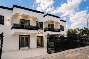 A modern two-story building with a white facade, black-framed windows, and a gated entrance. - Modern Luxury • Gym • Fast WiFi • Parking (Santiago De Los Caballeros)