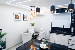 Cocina moderna con comedor, que incluye iluminación colgante, encimera negra y muebles de cocina blancos.