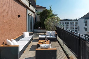 Une terrasse sur le toit avec des sièges en plein air, une table avec une bouteille et des verres, et une vue sur les bâtiments environnants.