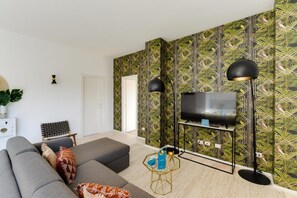 Una sala de estar moderna con un sofá gris, un televisor de pantalla plana sobre un mueble bajo y un papel tapiz estampado.