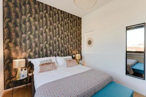 Habitación de hotel con una cama grande, un espejo, una mesita de noche y papel tapiz con plumas de pavo real.