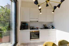 Una cocina moderna con armarios blancos, horno empotrado, pileta y cafetera negra.