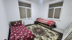 A bedroom with two beds, a patterned rug, and windows with blinds. - Standart 3 Bedroom Flat for Groups & big Families (Tashkent)