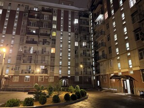 A multi-story residential building with balconies, a gated entrance, and a small landscaped area with shrubs. - Standart 3 Bedroom Flat for Groups & big Families (Tashkent)
