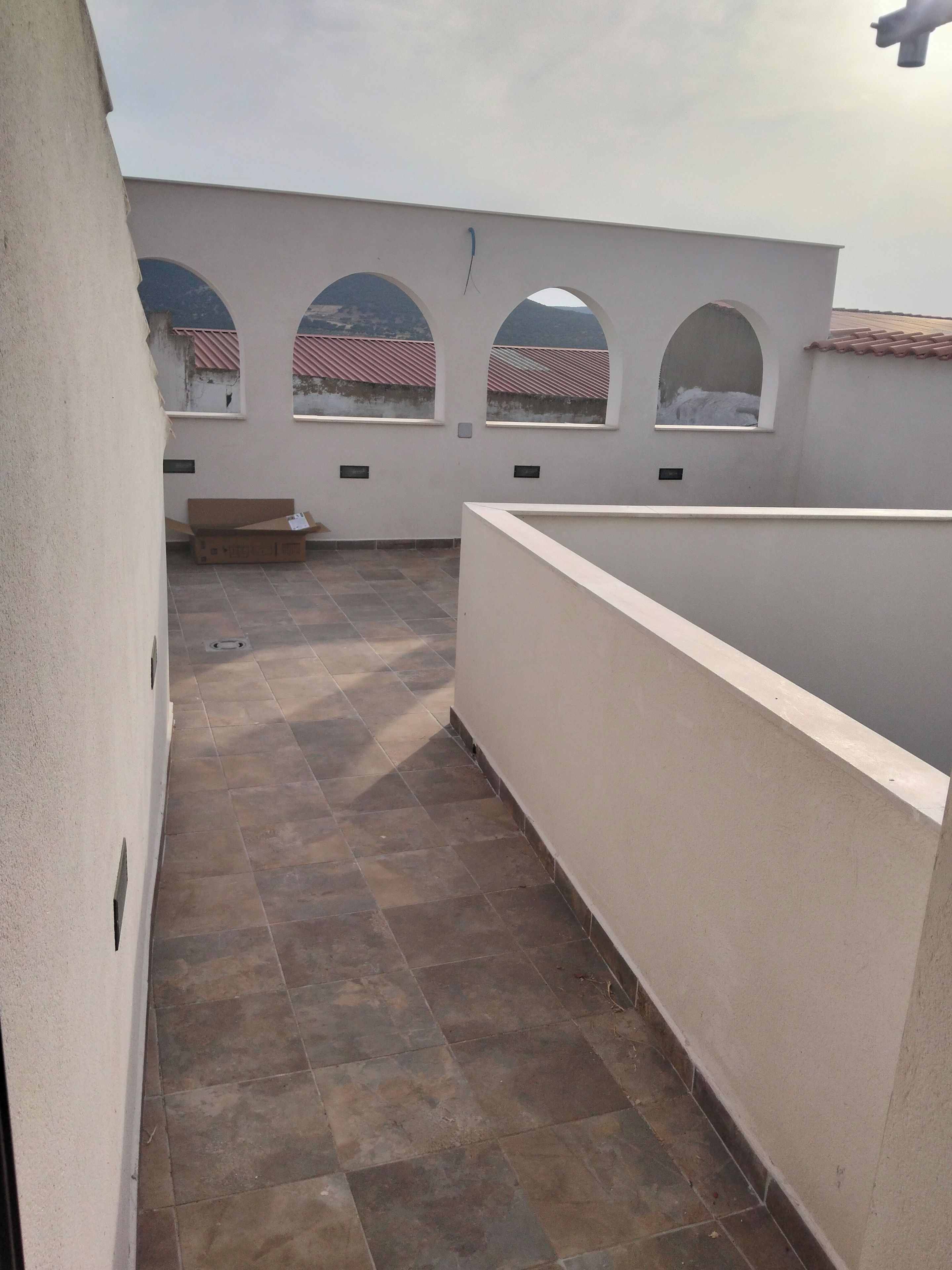 Un couloir carrelé qui mène à un balcon doté de fenêtres en arc de cercle.