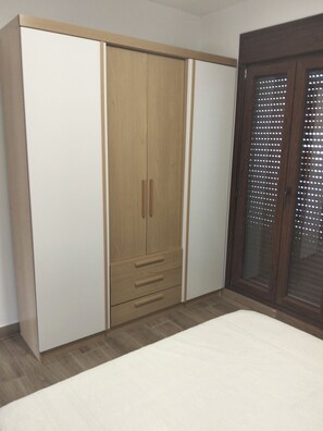 A bedroom with a wardrobe, a bed, and a door with a window.