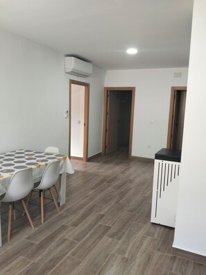 Un coin repas avec une table et des chaises, une kitchenette et un couloir menant à une autre pièce.