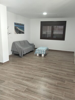 Une pièce avec un lit, une petite table, une fenêtre avec des stores et un tableau au mur.