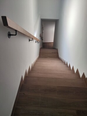A staircase with wooden steps and a handrail, leading to a landing with a wooden shelf and a wall-mounted light fixture.