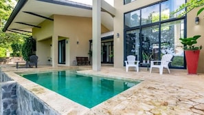 A swimming pool with a stone deck, surrounded by a covered patio area with chairs and potted plants. - Casa Ironbark (Potrero)