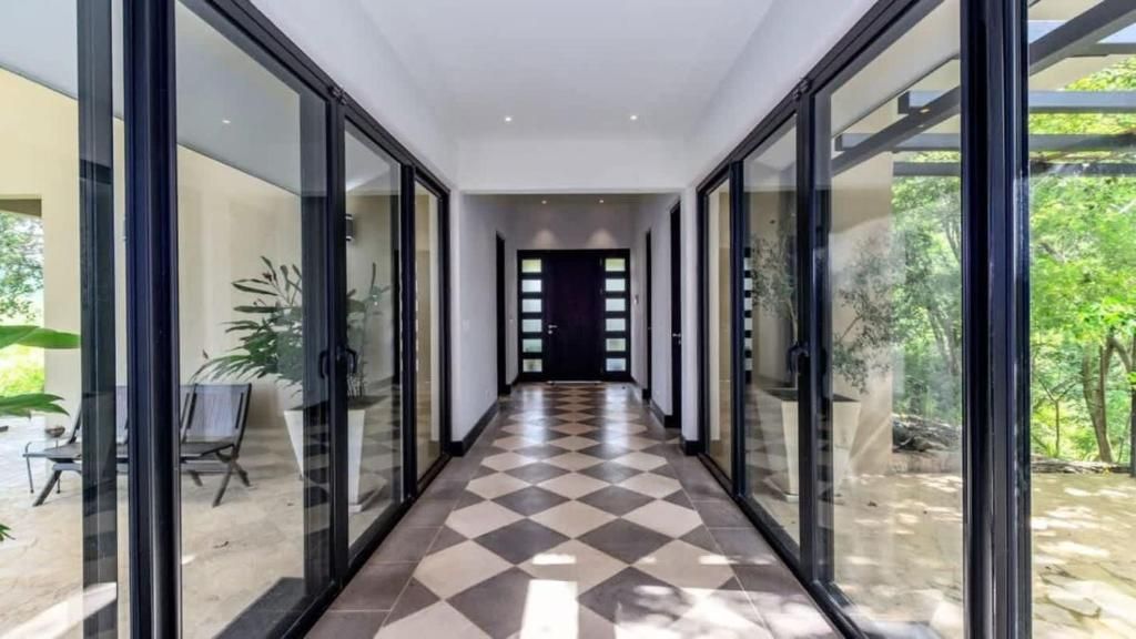 A corridor with glass doors leading to outdoor areas, a tiled floor, and a view of greenery outside.