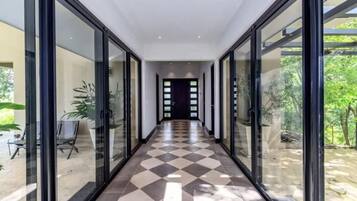 A corridor with glass doors leading to outdoor areas, a tiled floor, and a view of greenery outside.
