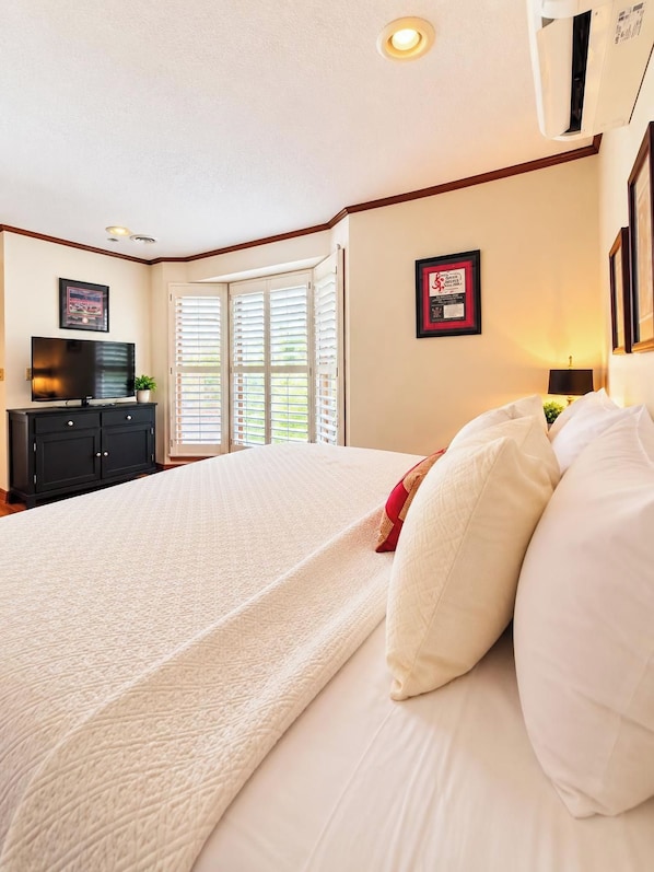Una habitación de hotel con una cama grande, televisor, cómoda y ventana con persianas.