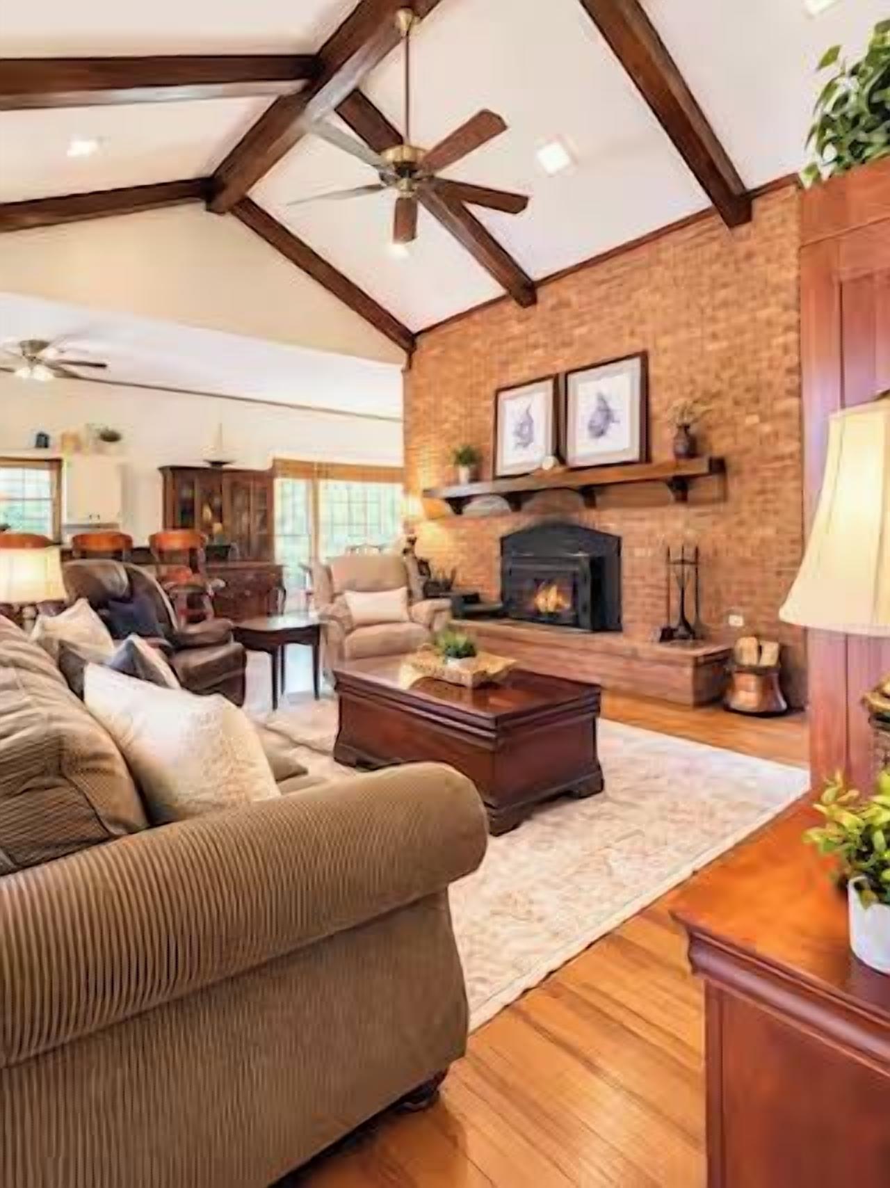 A living room with a fireplace, wooden flooring, and a ceiling fan.