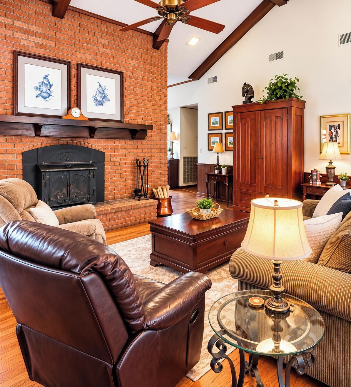 A living room with a brick fireplace, leather chairs, a glass coffee table, and framed artwork on the walls.