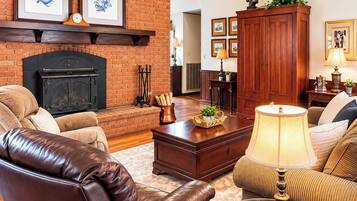 A living room with a brick fireplace, leather chairs, a glass coffee table, and framed artwork on the walls.
