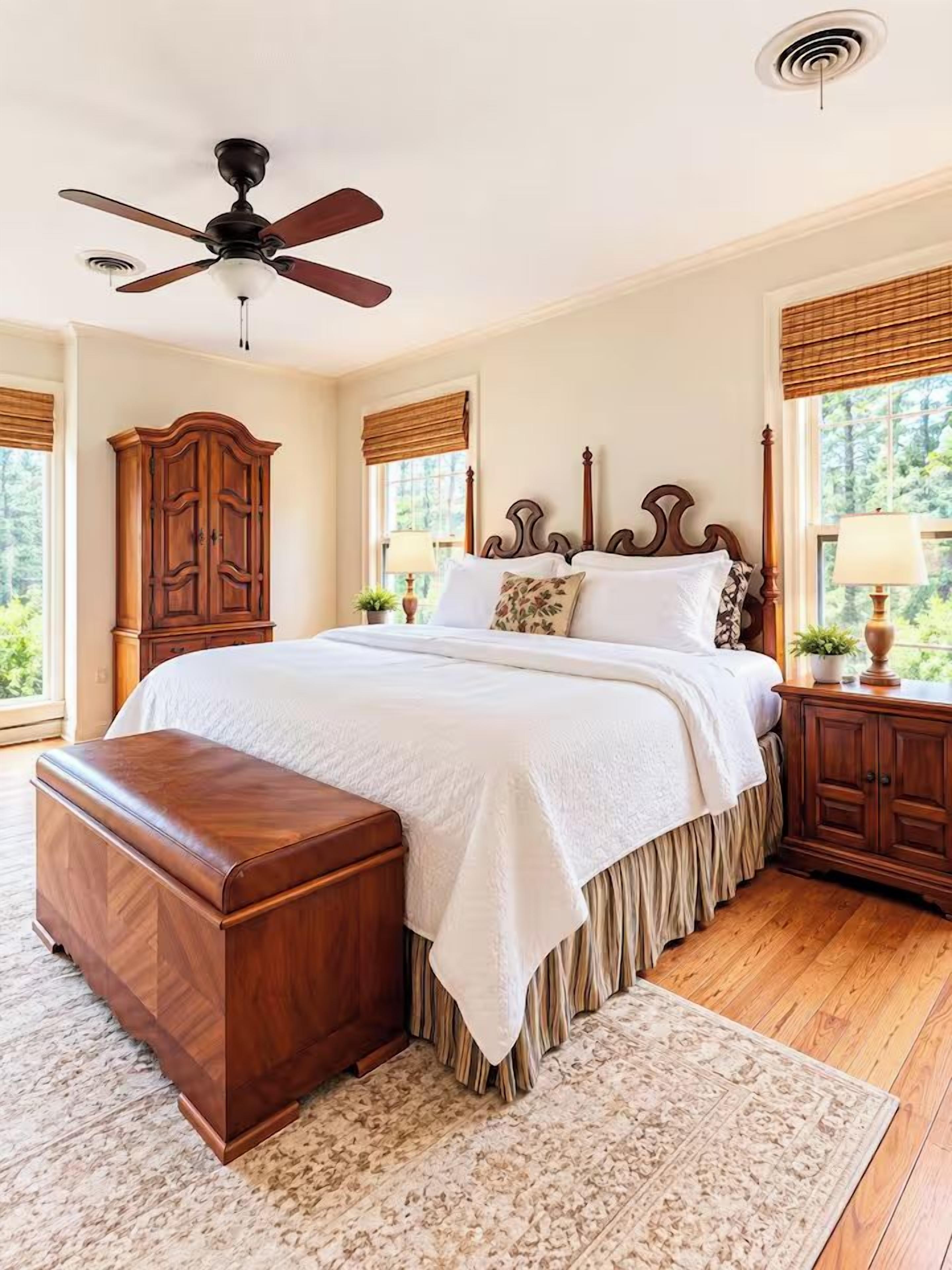 Une chambre à coucher comprenant un lit, un banc en bois, un ventilateur de plafond, une table de chevet et une fenêtre donnant sur un paysage verdoyant.