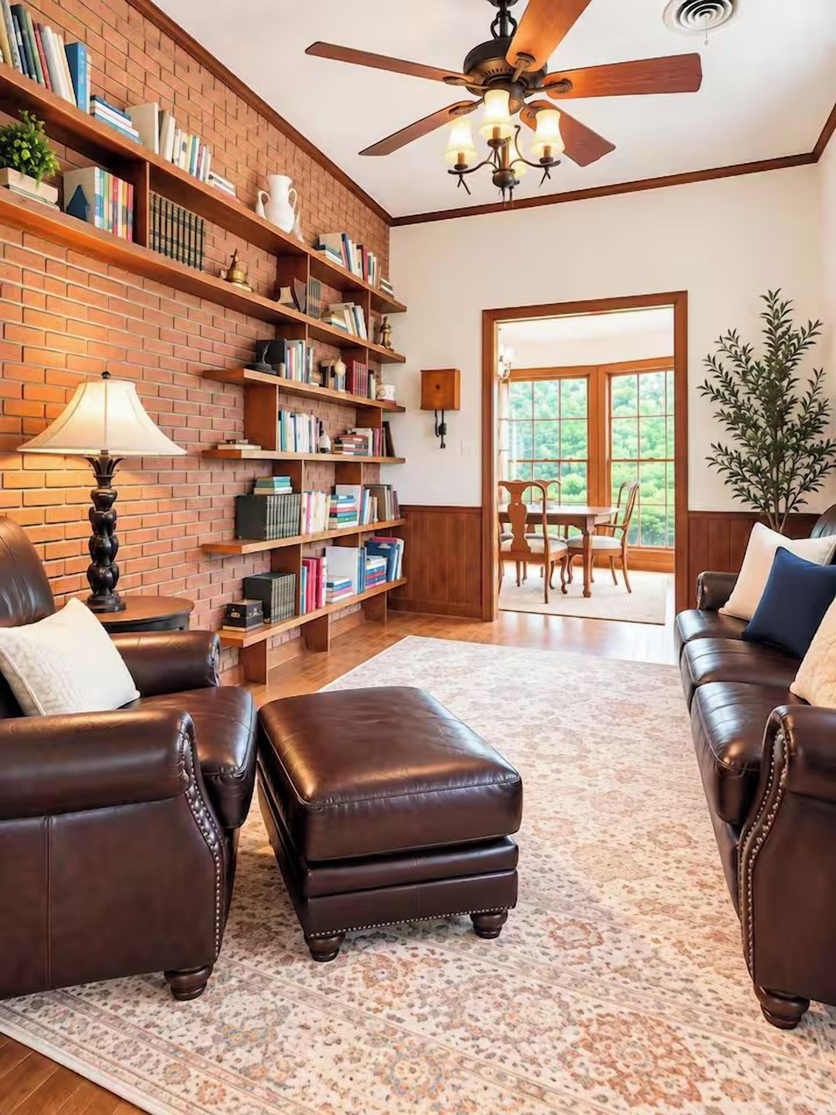 A living room with leather sofas, a coffee table, a fireplace, bookshelves, and a dining area with a view.