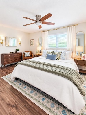 A bedroom with a bed, a ceiling fan, a nightstand, a dresser, and a window with curtains.