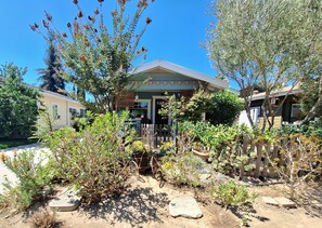 A residential property with a front porch, a wooden fence, and various plants. - Charming 2-Bdrm Historic Bungalow~ Hummingbird Garden & HotTub in DT Fullerton! (Fullerton)