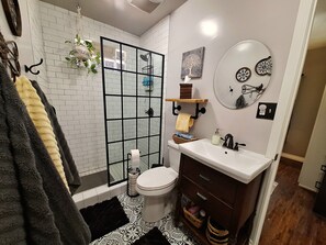 Ein Badezimmer mit einer weißen Duschkabine, einer Toilette, einem Waschbecken mit Spiegel und einem Holzkorpus.