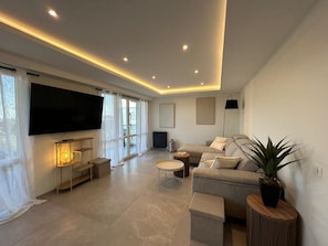 A modern living room with a flat-screen TV, sofa, coffee table, and a potted plant. - Beautiful, air-conditioned 2-bedroom apartment with a sea view in a quiet neighborhood (Saint Raphaël)
