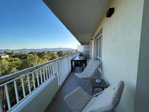 A balcony with a table and two chairs, overlooking a cityscape with distant mountains. - Beautiful, air-conditioned 2-bedroom apartment with a sea view in a quiet neighborhood (Saint Raphaël)