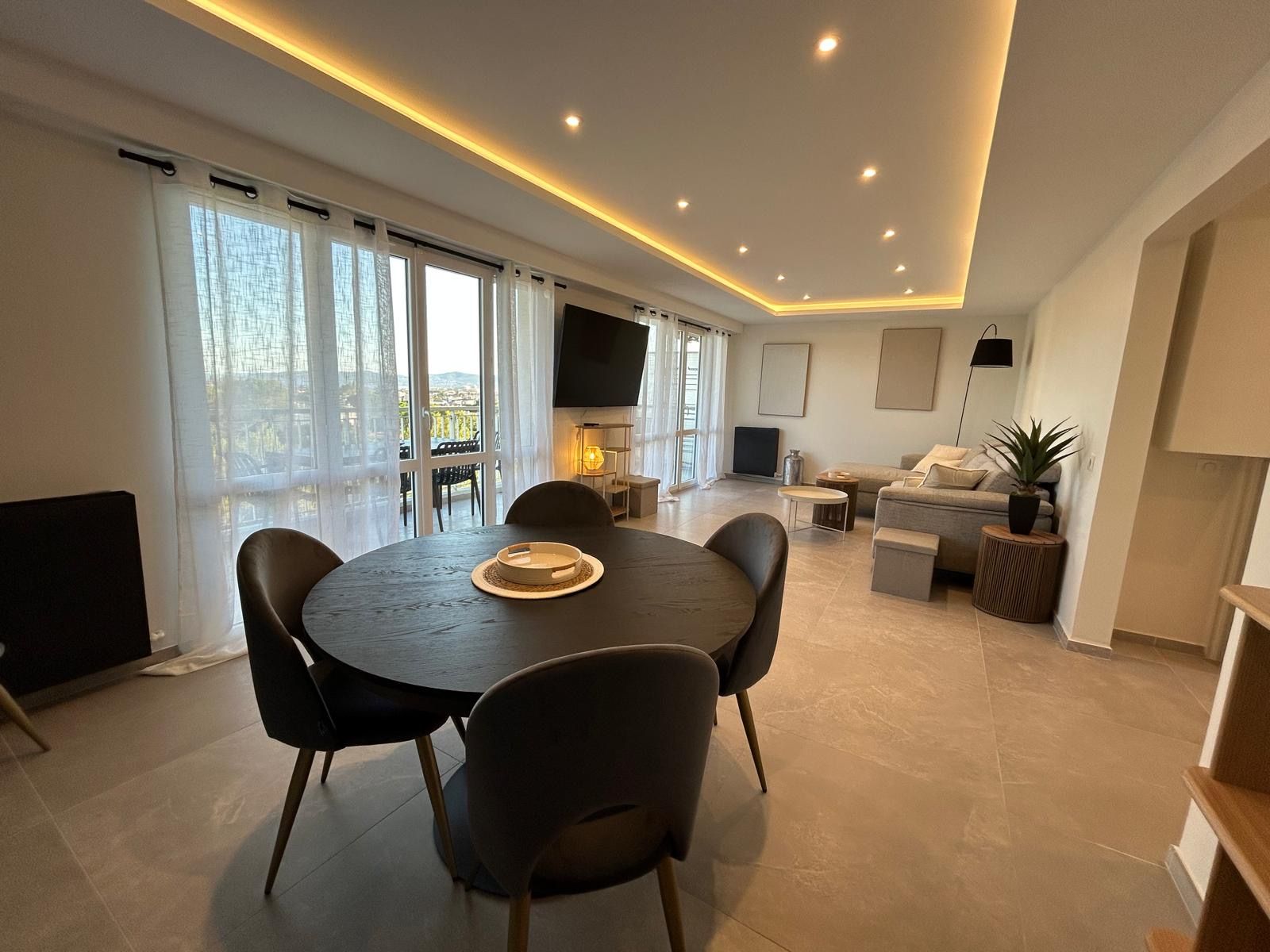 A modern living room with a round table, chairs, a sofa, a TV, and a balcony with curtains.