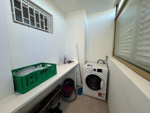 A laundry room with a washing machine, a drying machine, a green basket, and a mop. - Beautiful, air-conditioned 2-bedroom apartment with a sea view in a quiet neighborhood (Saint Raphaël)