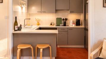 Una cocina moderna con armarios grises, una encimera blanca, dos taburetes de madera y un lavavajillas integrado.