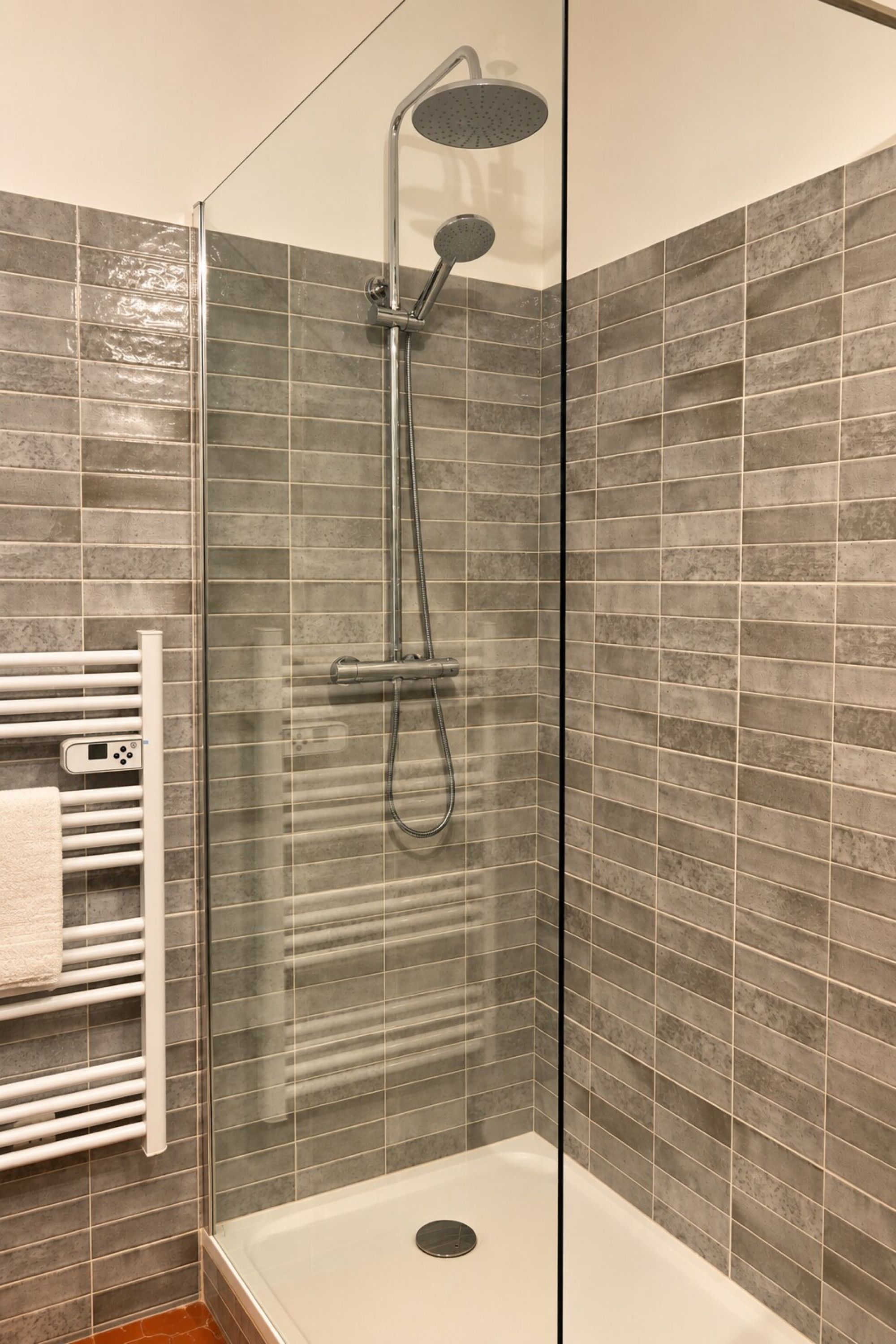 Een douche met een handdouche en een wandmengkraan, afgesloten met een glazen deur.