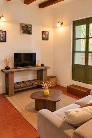 Un salon avec un téléviseur posé sur un meuble en bois, un canapé, une table basse et une fenêtre donnant sur un paysage verdoyant.